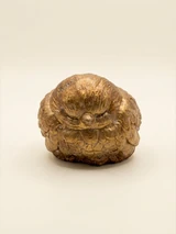 Rounded sleeping bird figure with a small beak and a layered feather pattern. Bronze and gold tones with a visible concrete texture.