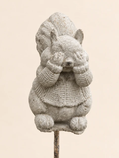 Light squirrel in a patterned sweater with its hands over its eyes, on a slender stake