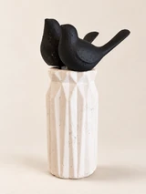 Two matte black birds with simple forms and upturned tails in a tall, white vase. From another angle.
