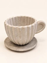 Close-up of a light ribbed decorative cup with a wavy rim, a cast handle and a saucer