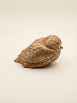 Rounded sleeping bird figure with a small beak and a layered feather pattern. Bronze and gold tones with a visible concrete texture.