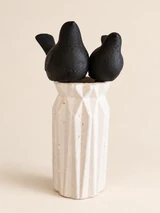 Two matte black birds with simple forms and upturned tails in a tall, white vase. From the front.