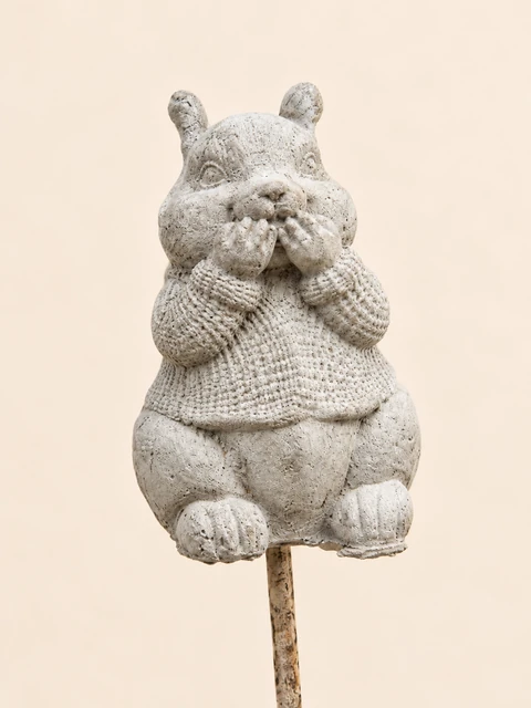 Light squirrel in a patterned sweater with its hands at its mouth, on a slender stake
