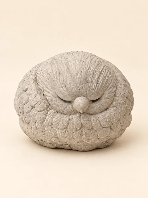 Rounded sleeping bird figure in concrete colour with closed eyes and a layered feather pattern