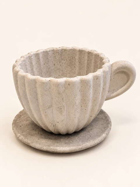 Close-up of a light ribbed decorative cup with a wavy rim, a cast handle and a saucer