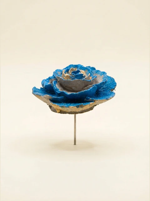 Blue and gold rose on a stake with layered petals and visible concrete texture.