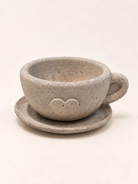 Rounded cast decorative cup with a raised heart at the front, a curved handle and a saucer