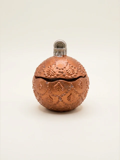 Spherical decorative container with a lid, a silver loop and raised fir trees and bead garlands. Copper and bronze colours with a visible concrete texture.