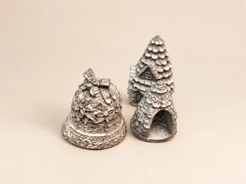 A silver Christmas bell and a tree form with an arched opening, with a house and fir tree behind