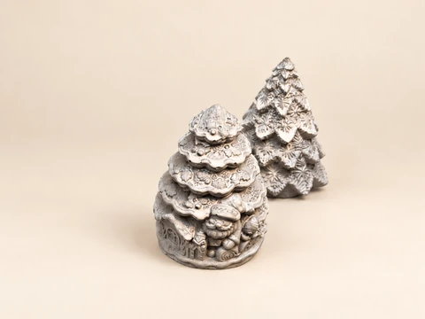 A silver Christmas tree with figures and another tree with a leaf pattern behind