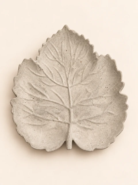 Shallow leaf plate in concrete colour with branching veins, an irregular edge and a short stem, seen from above